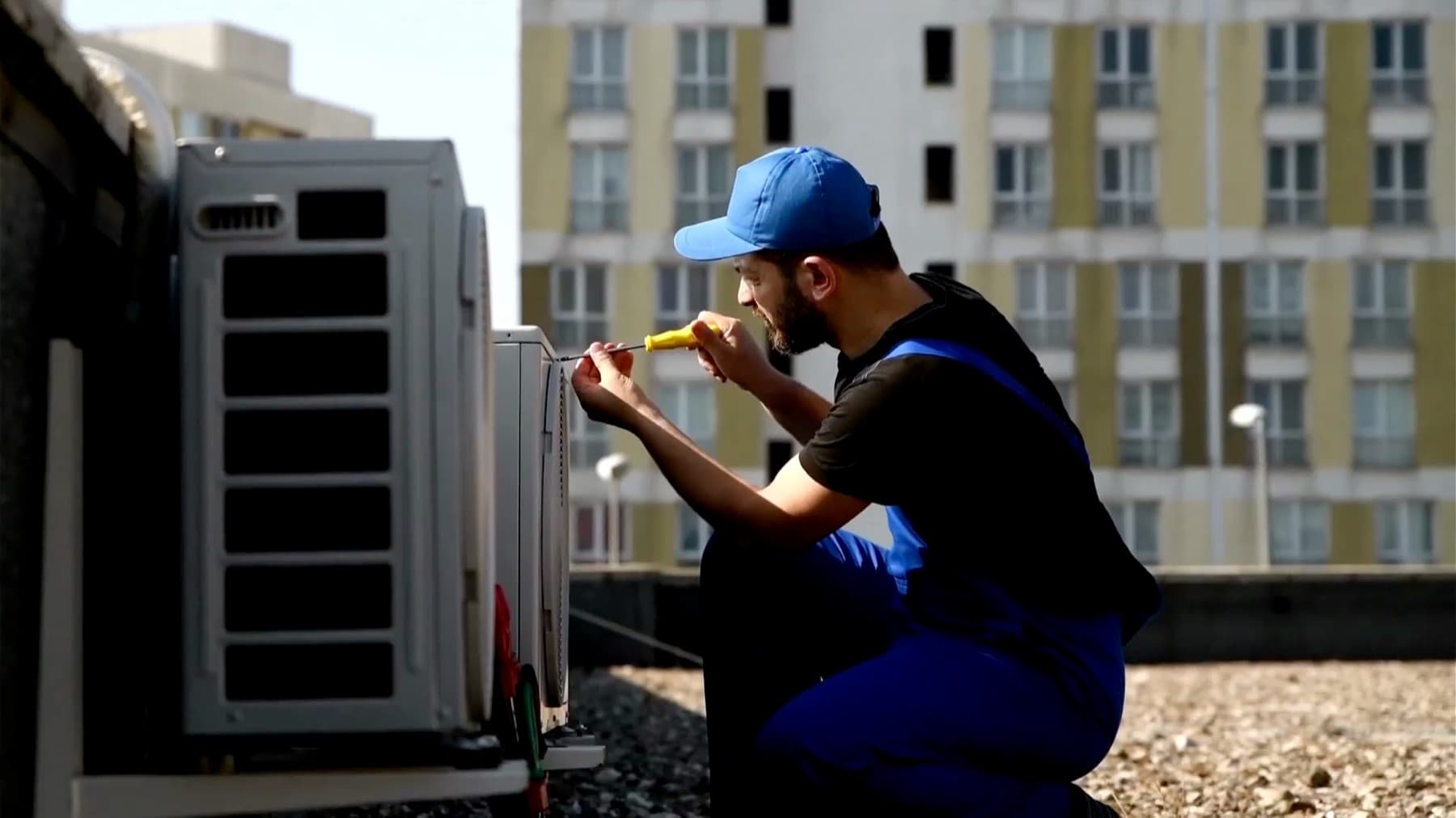 Técnico ajustando con un destornillador la unidad exterior de un aire acondicionado en la cubierta de un edificio