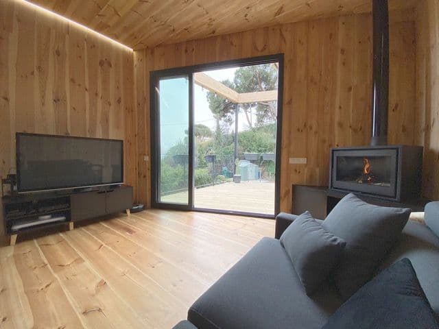 Salón revestido de madera con una estufa de leña tipo casete en la esquina y salida al jardín