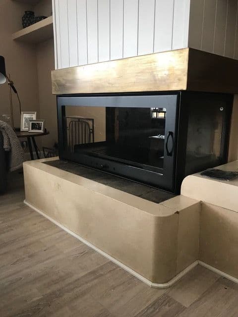 Chimenea de leña cerrada con puertas de cristal a medida sobre una bancada curva de obra