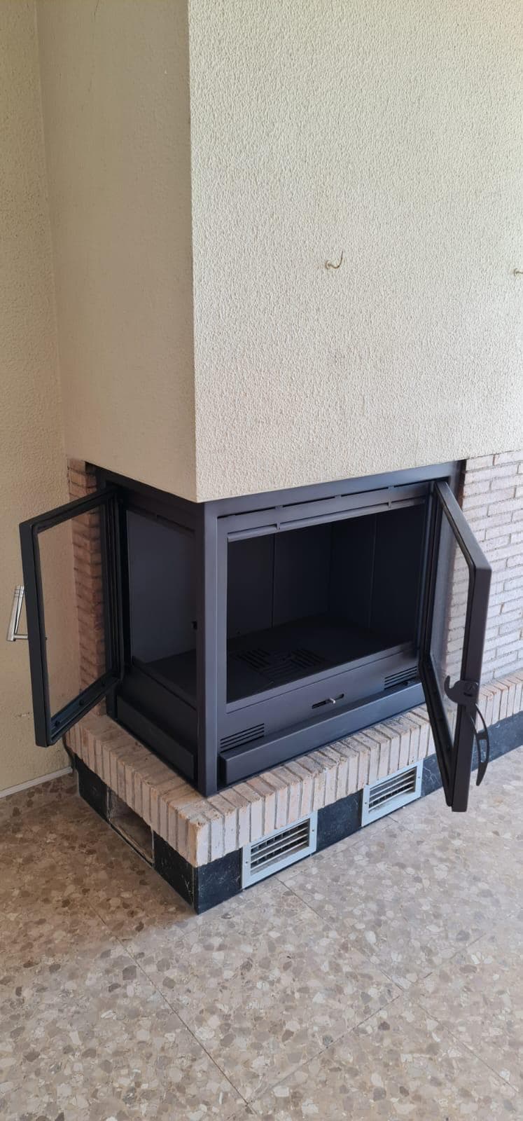 Chimenea de leña con el cerramiento de cristal a medida y la puerta abierta para cargar la leña