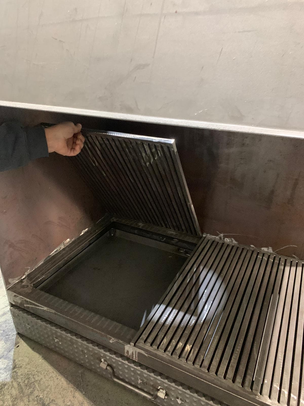 Parrilla de un casete de leña hecho a medida levantada para acceder a las cenizas