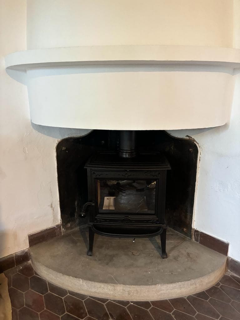 Estufa de leña clásica negra colocada dentro de una chimenea antigua con campana blanca